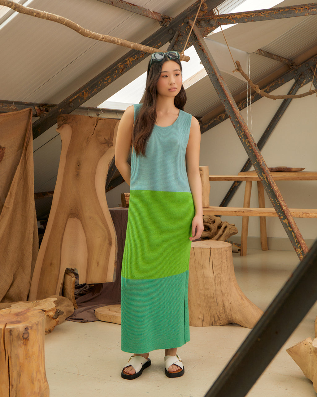 Woman wearing a Elegant Colour Block Belted Slit Dress in Green & Blue - Sustainable Wool & Cashmere, Made in London standing in a rustic wooden interior.