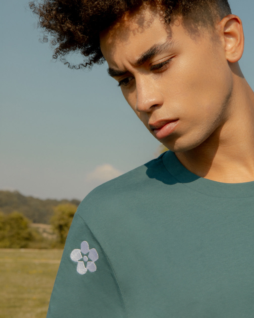 Man wearing a Symbols Embroidered Organic Cotton Teal Sustainable T-Shirt in a field