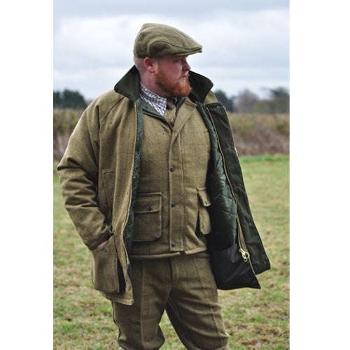 Man wearing a traditional Game Tweed Jacket outfit with a jacket, pants, and flat cap in an outdoor setting.