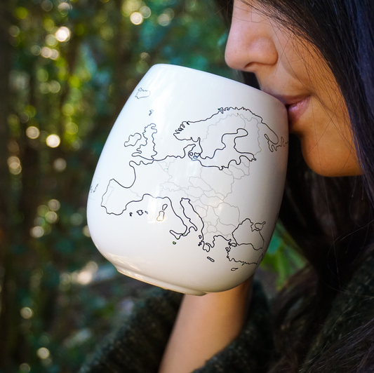 Person drinking from a white mug with a world map design against a blurred green background