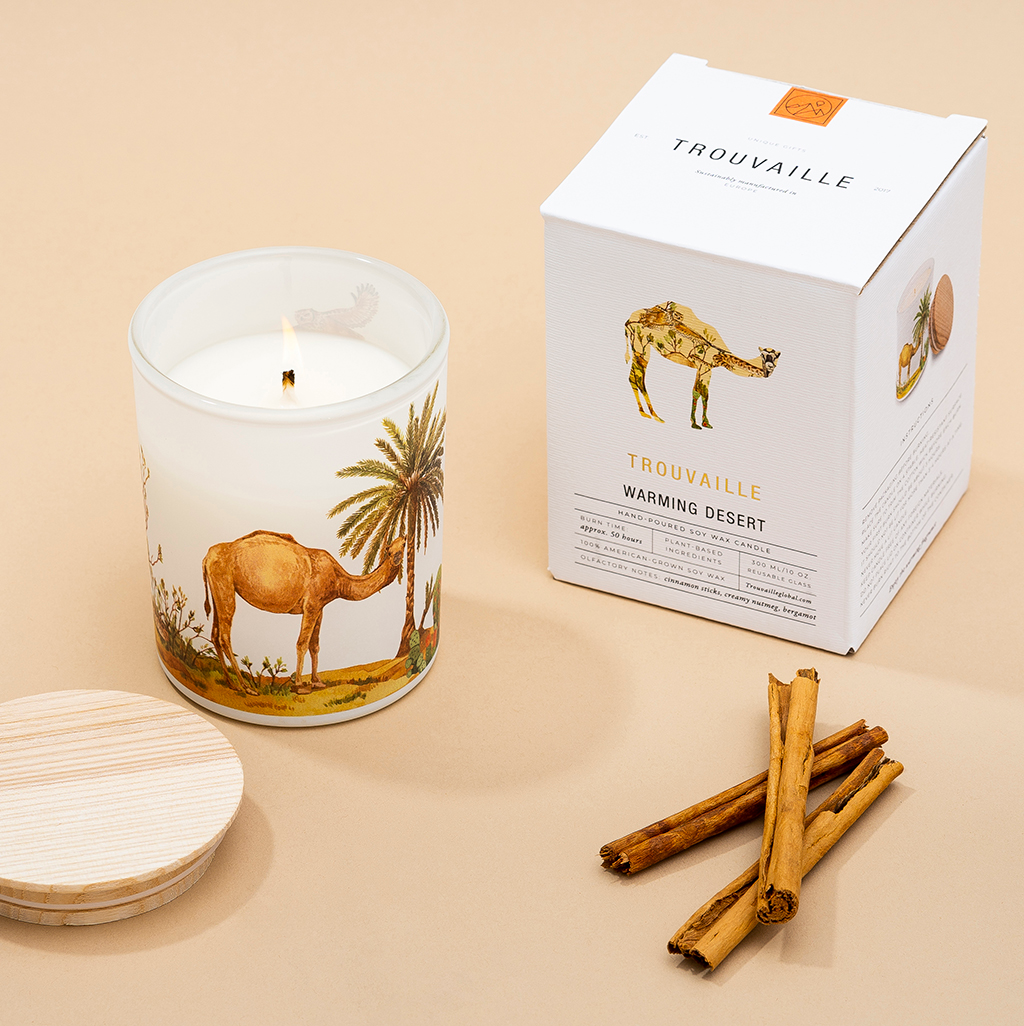 Candle with camel design, packaging, and cinnamon sticks on a beige background