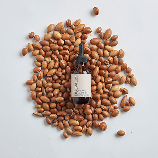 Douval's organic argan oil bottle surrounded by argan seeds on a light gray background