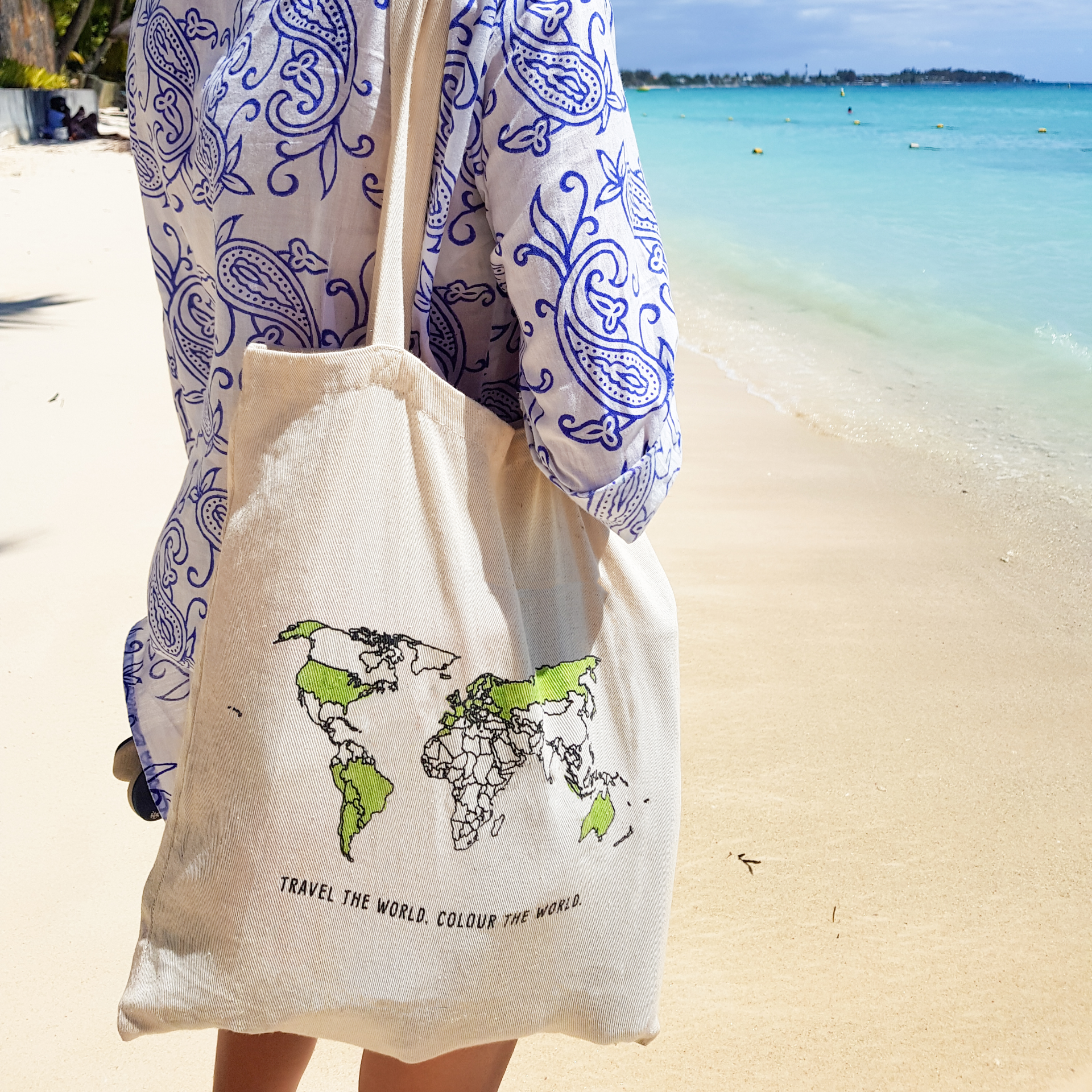 Person holding a tote bag with a world map design on a beach.