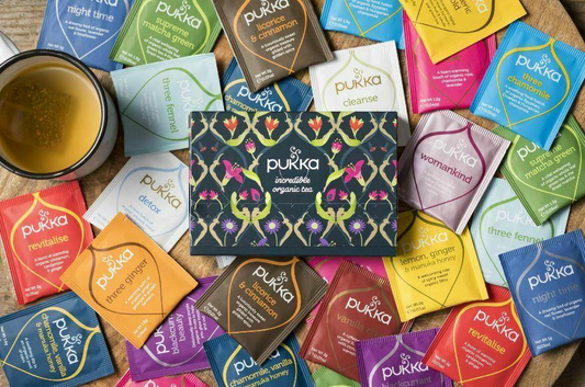 Assorted Pukka tea bags on a wooden surface with a cup of tea.