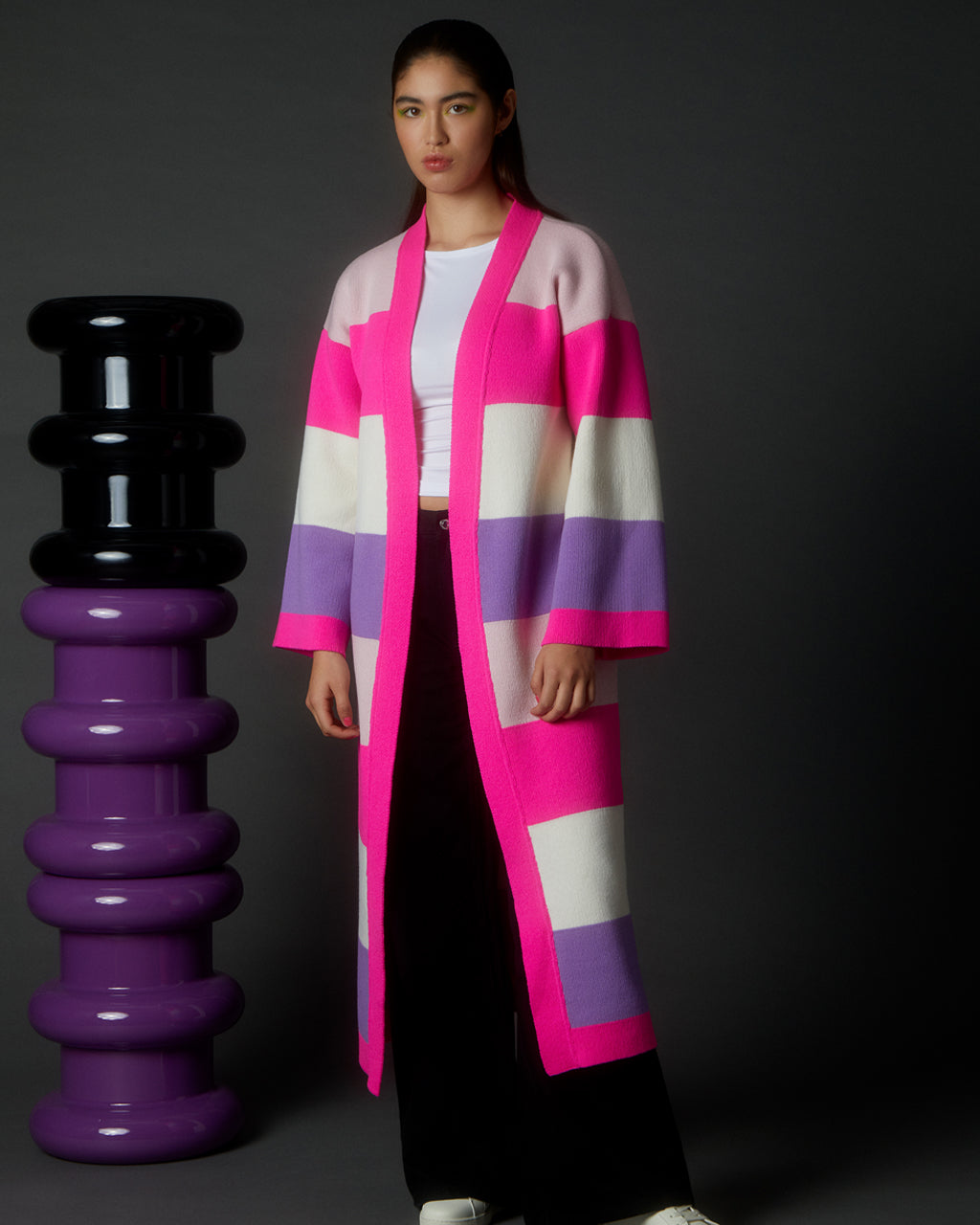Woman wearing a Luxurious Multicolour Striped Long Cardigan - Wool & Cashmere Blend | Sustainable & Cozy standing next to a black and purple sculpture on a dark background