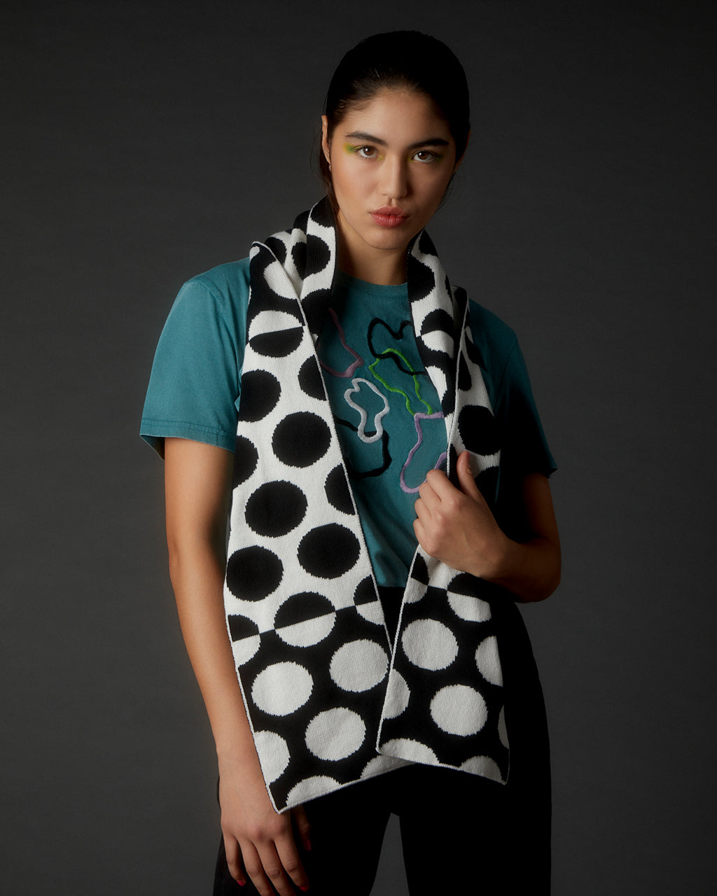 Design Your Own Scarf - Personalized, Reversible & Sustainable Fashion | Customizable Knit Scarf. Person wearing a black and white polka dot scarf with a dark background
