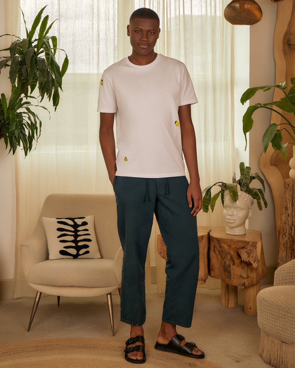 Man standing wearing a Lemon Embroidered Organic Cotton T-Shirt | Eco-Friendly & Stylish Crew Neck in a stylish living room with plants and furniture.
