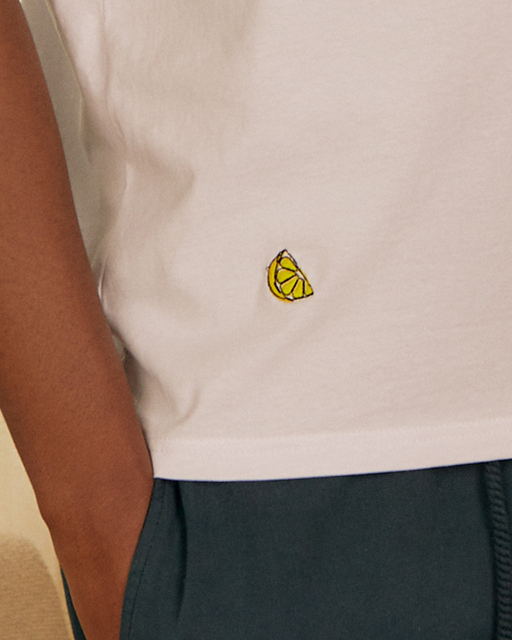 Close-up of a person wearing a white Lemon Embroidered Organic Cotton T-Shirt | Eco-Friendly & Stylish Crew Neck with a yellow lemon wedge