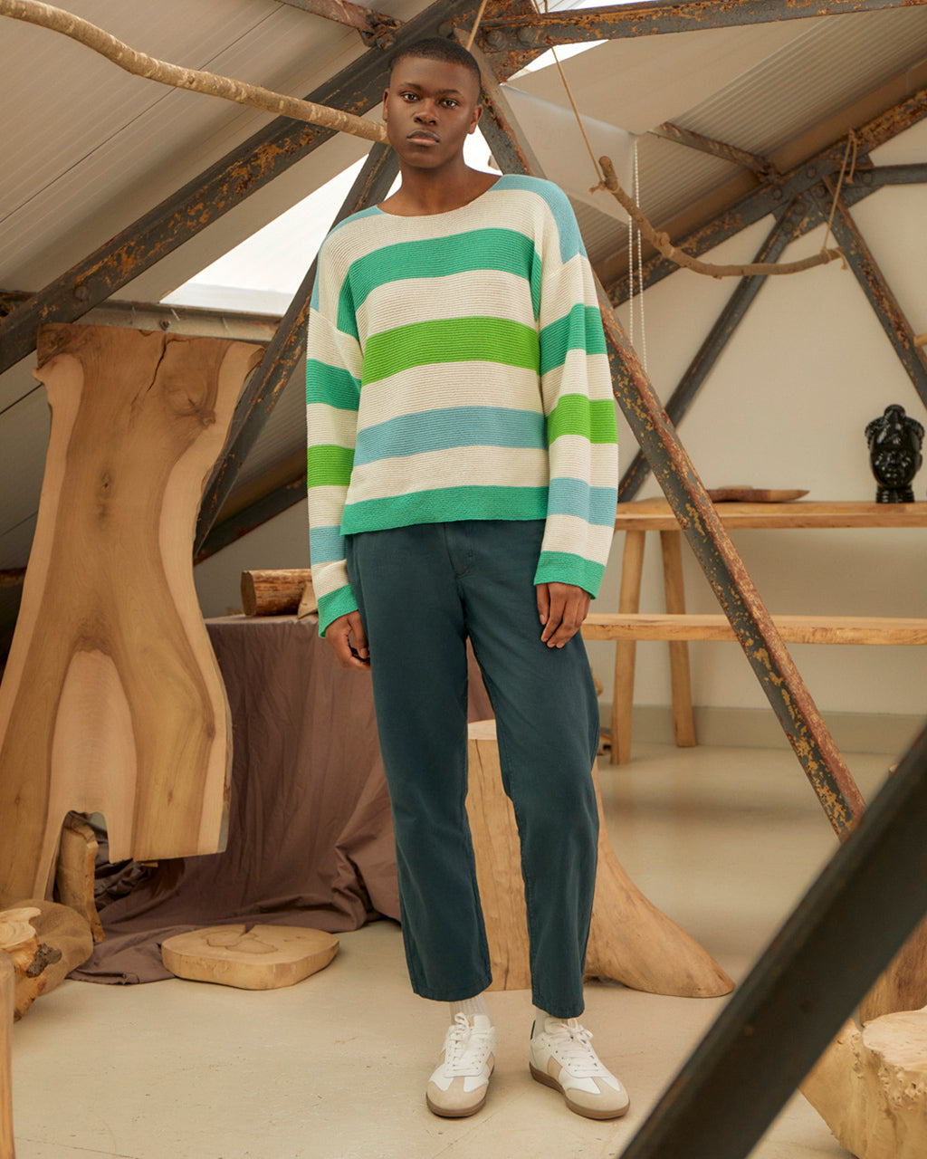 Man wearing a Eco-Friendly Striped Dropped Shoulder Top - Green & Blue | Wool & Cashmere Blend, Ethically Sourced and pants in a rustic indoor setting