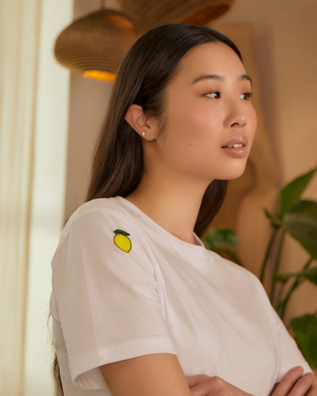 Woman wearing a Lemon Embroidered Organic Cotton T-Shirt – 100% Sustainable, standing indoors. Close up o embroidered lemon.
