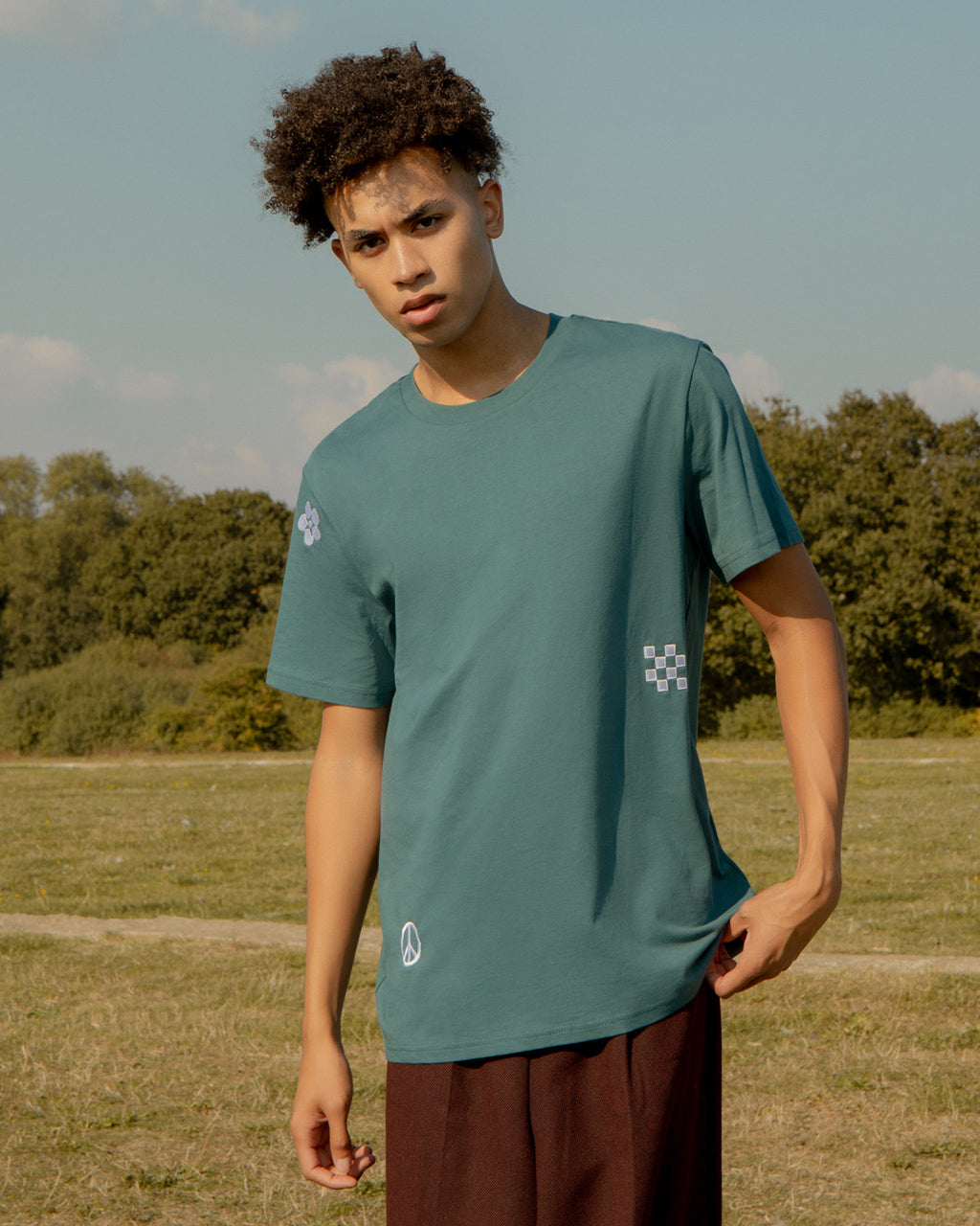 Person wearing a Symbols Embroidered Organic Cotton Teal Sustainable T-Shirt in an outdoor setting