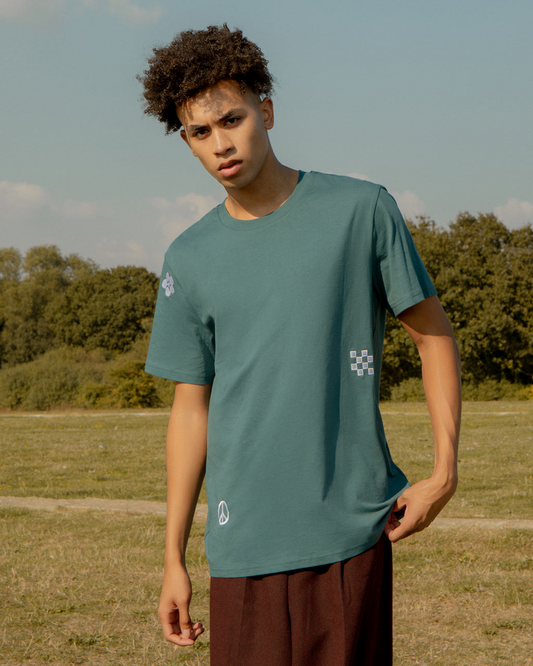 Person wearing a Symbols Embroidered Organic Cotton Teal Sustainable T-Shirt in an outdoor setting