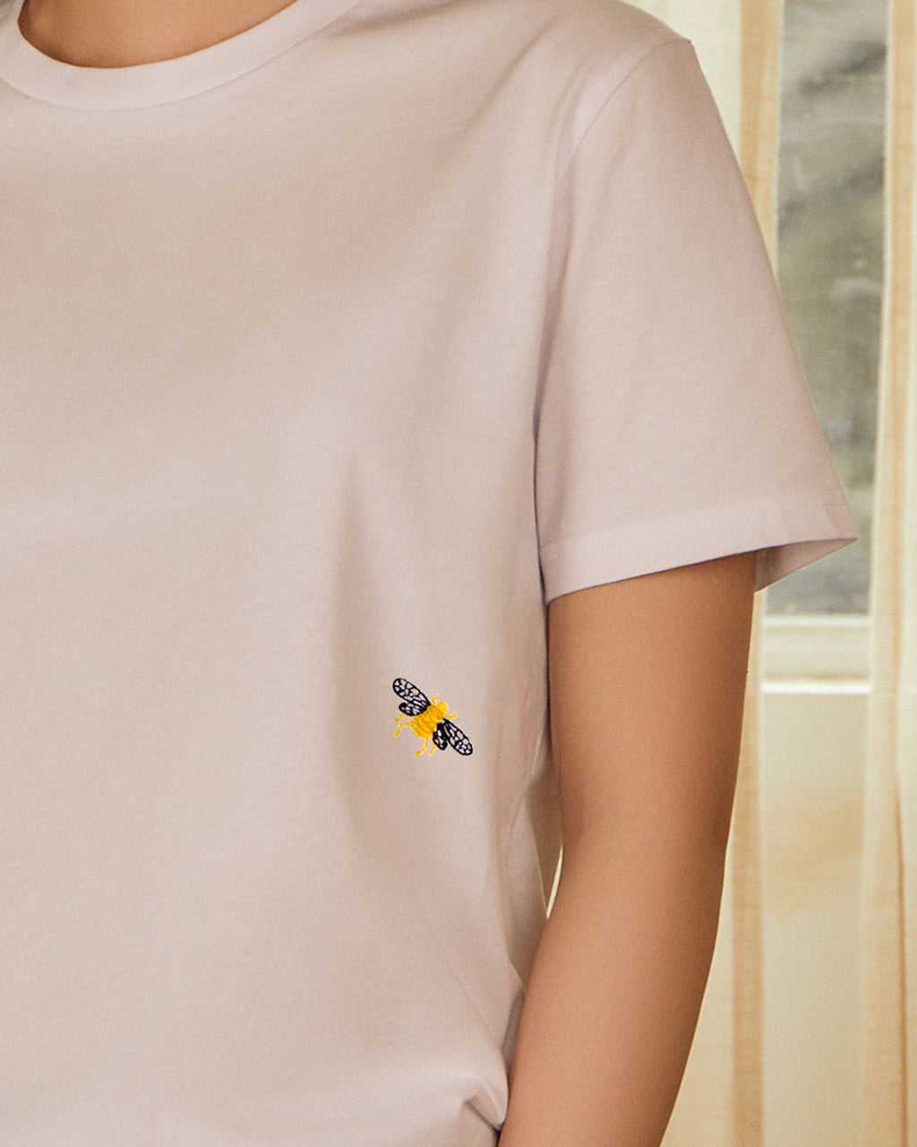 Close up of an embroidered bee on the Bee Embroidered Organic Cotton T-Shirt - Handmade in UK, Eco-Friendly with a window background