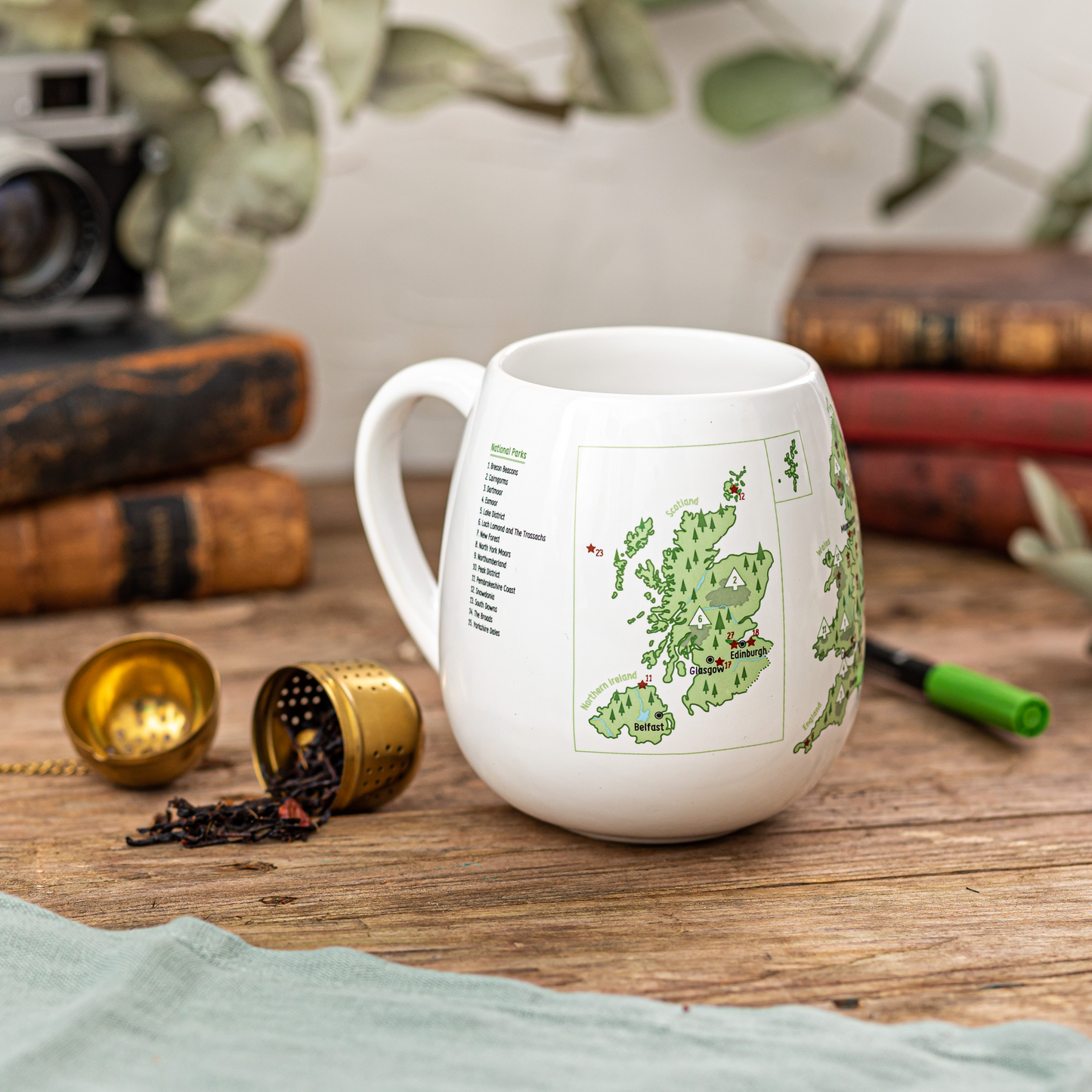 White mug with a map design on a wooden surface with books and tea accessories.