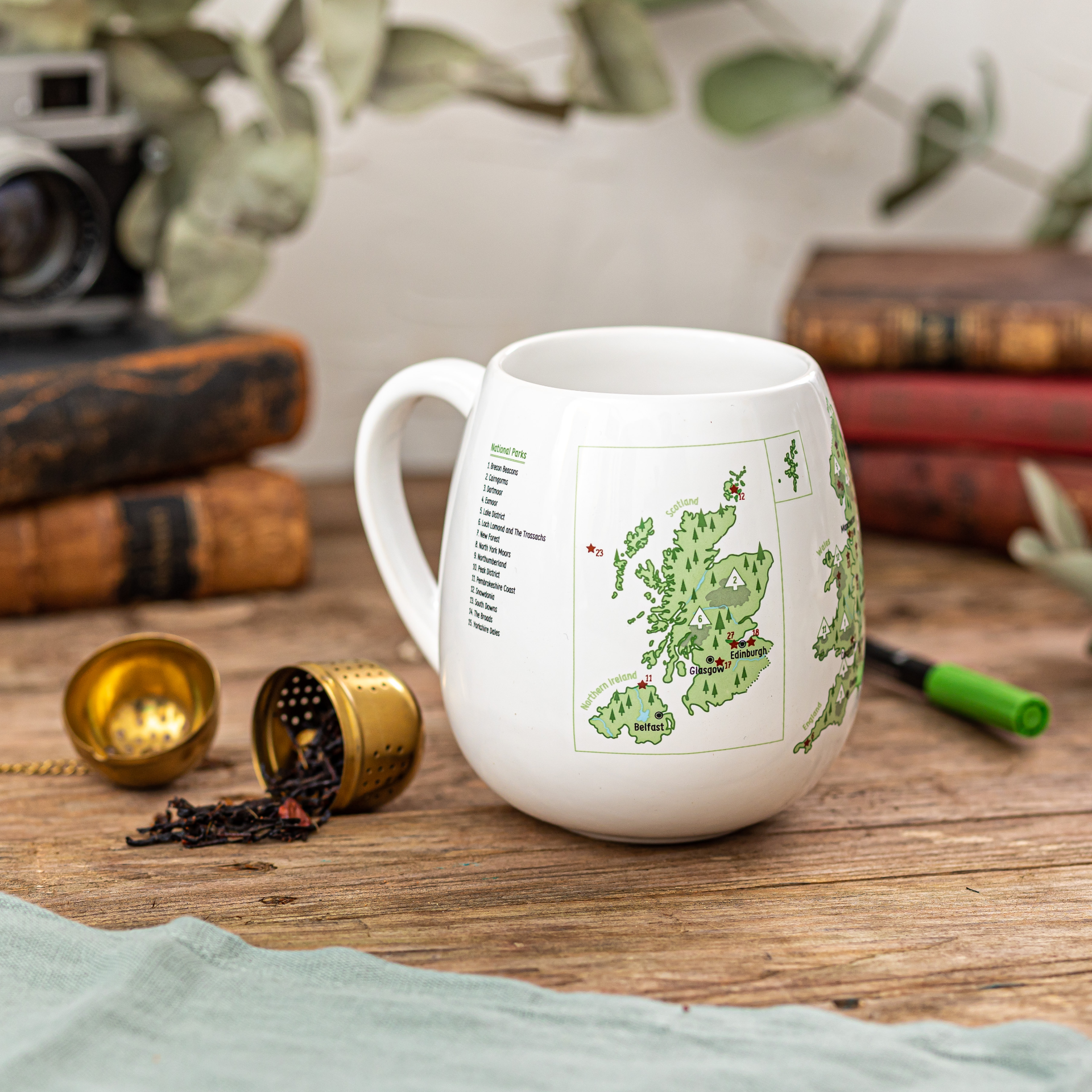 White mug with a map design on a wooden surface with books and tea accessories.