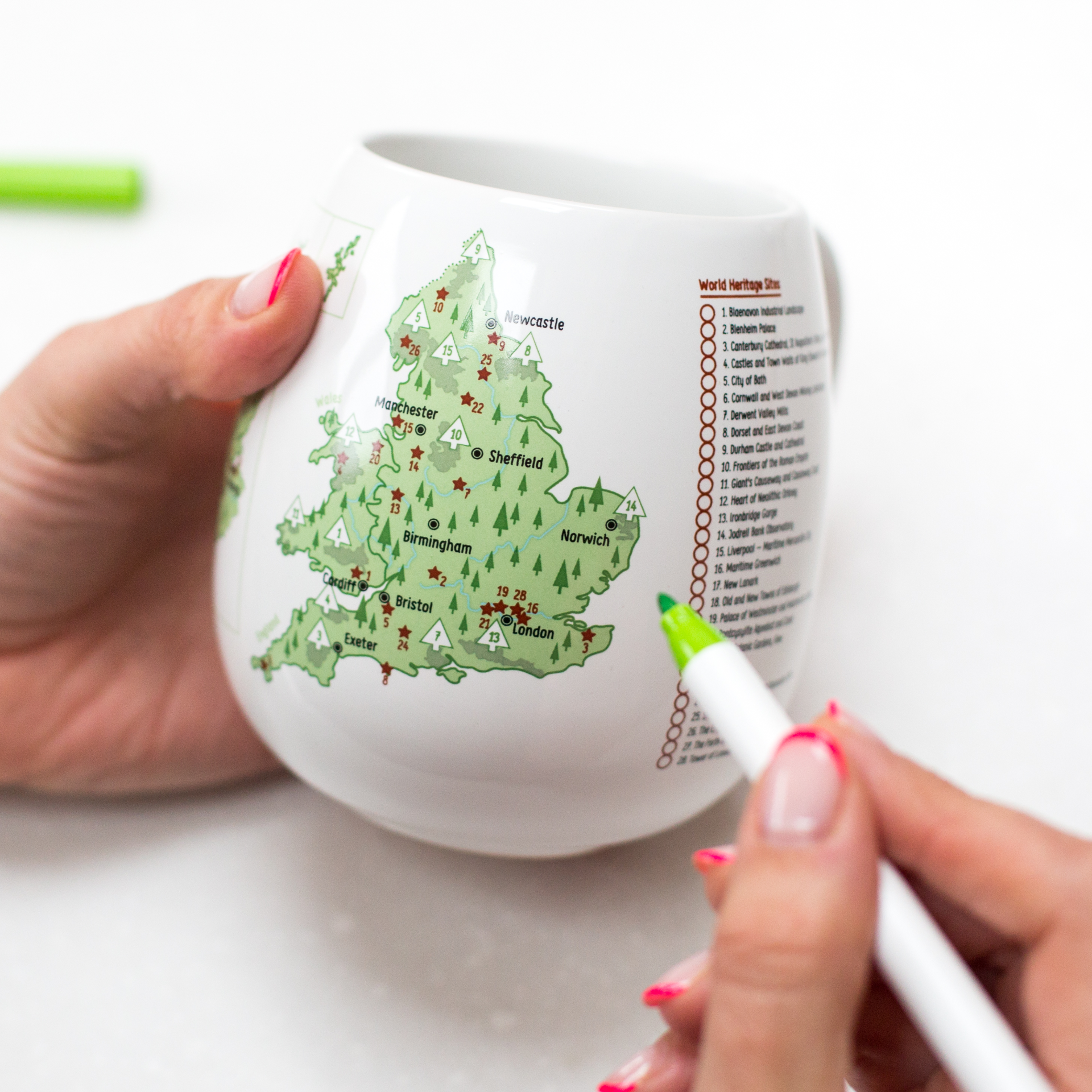 Person holding a mug with a map design and a pen, on a white background