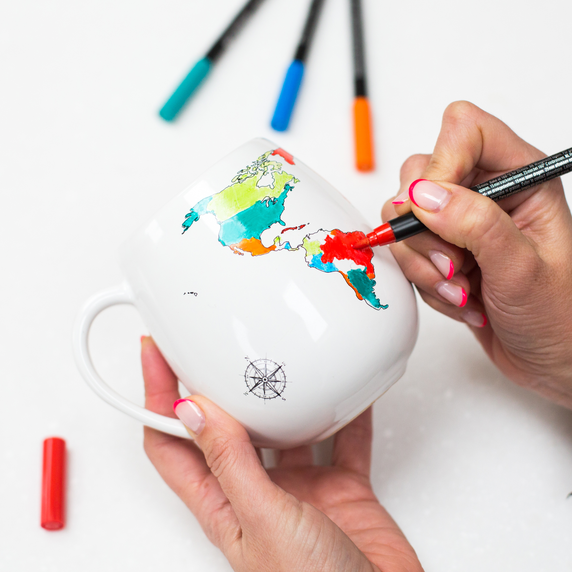 Person coloring a world map on a ceramic mug with markers.
