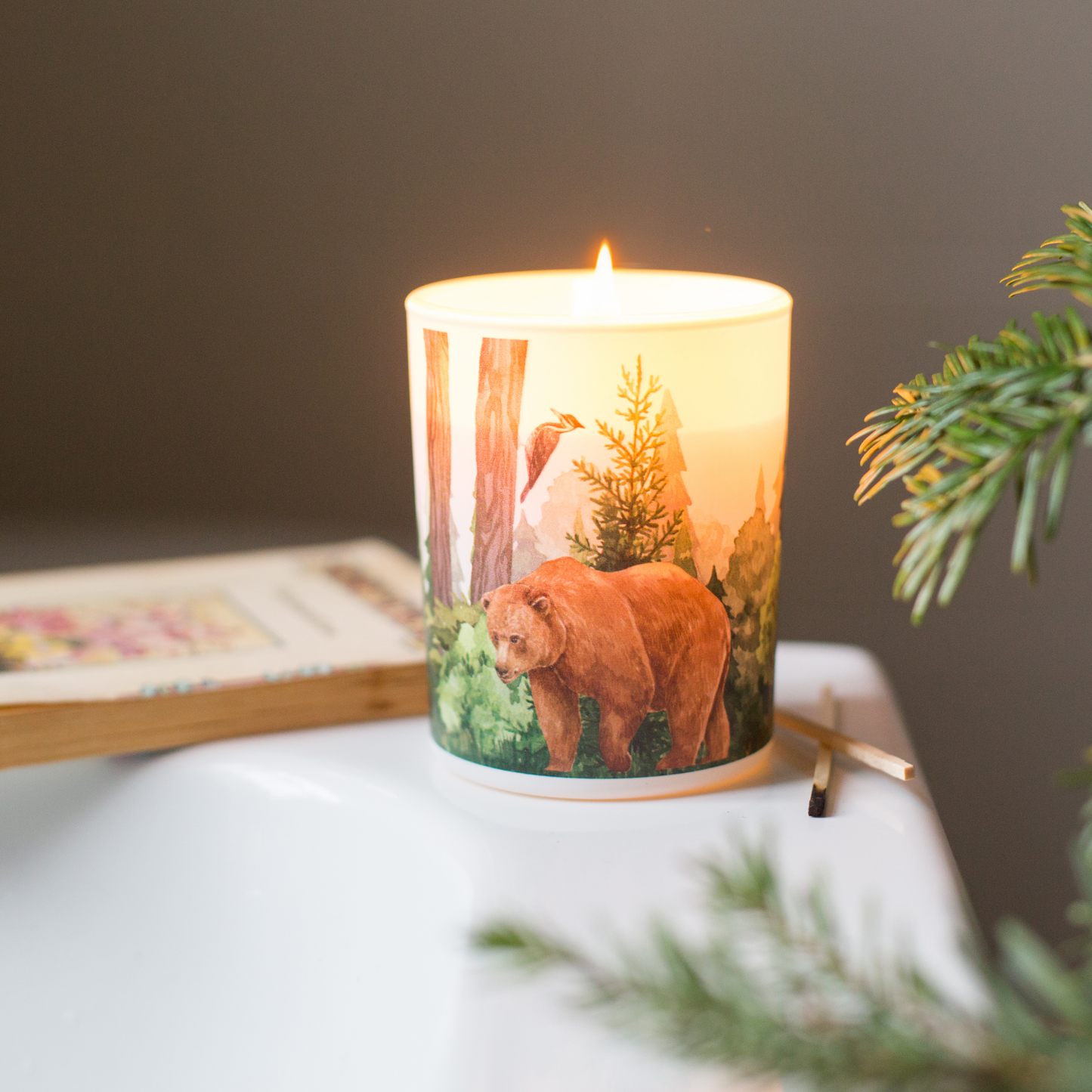 A lit scented candle with a bear design on a table with a blurred background
