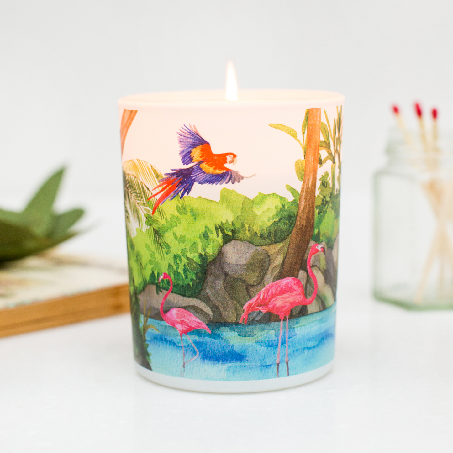 Candle with a colorful design of flamingos and a parrot on a white background