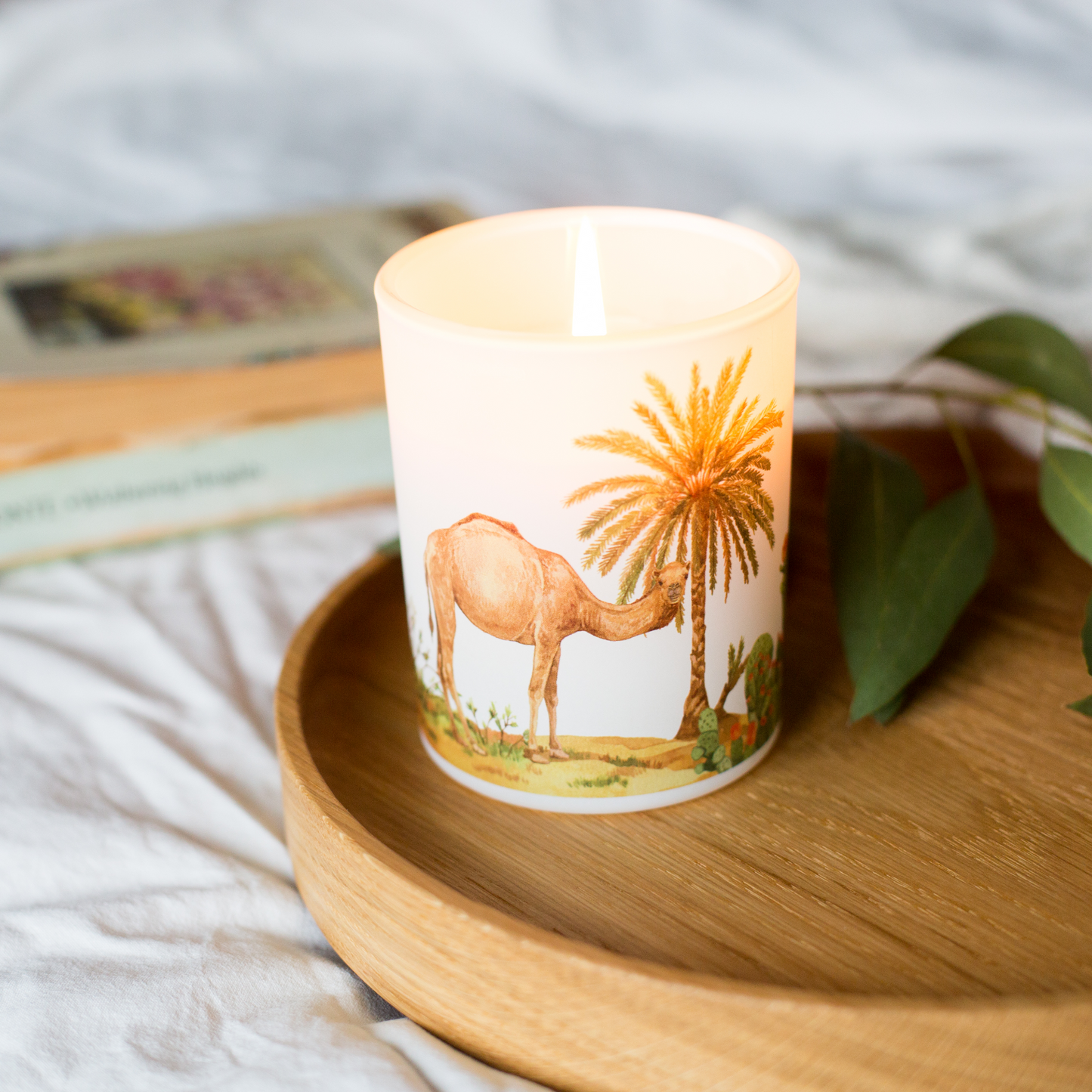 Candle with a desert scene design featuring a camel and palm tree on a wooden tray.