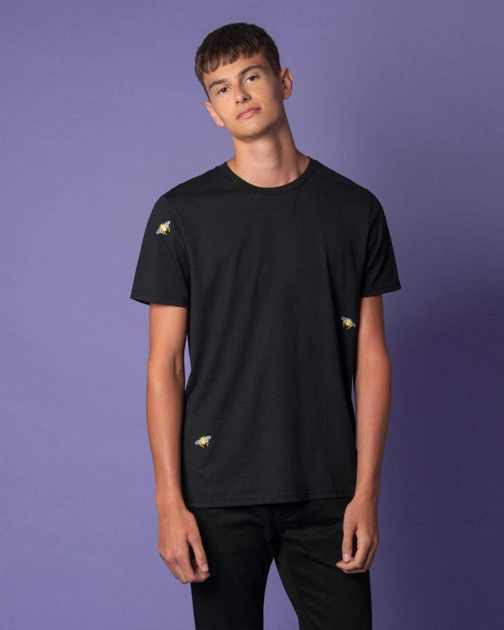 Person wearing a black Bee Embroidered Black T-Shirt with small yellow logos on a purple background